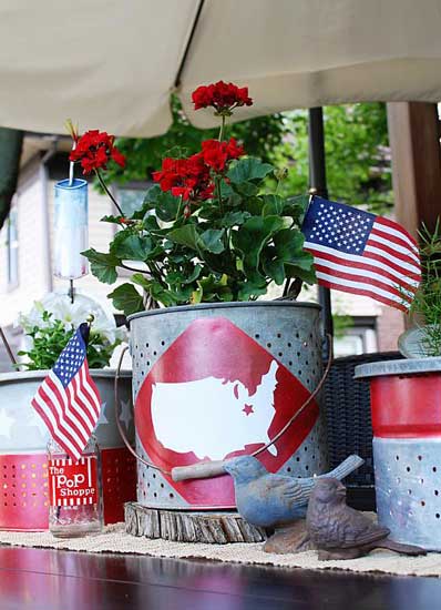 A rustic steel bucket used as a 4th of july centerpiece. A giant red circle is painted on the front with a white outline of the United States