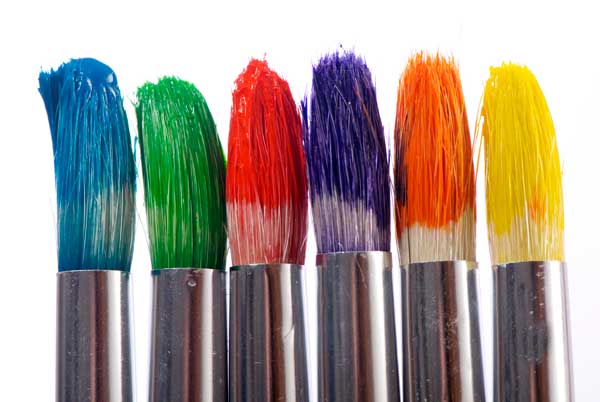 A close-up of the tips of paintbrushes all dipped in paint in order to make a rainbow.