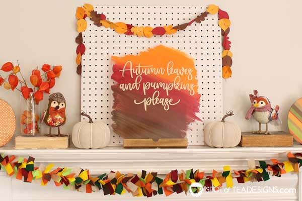 An acrylic sign painted in fall colors and hung over a fireplace along with some fall leaf garland for a festive look.