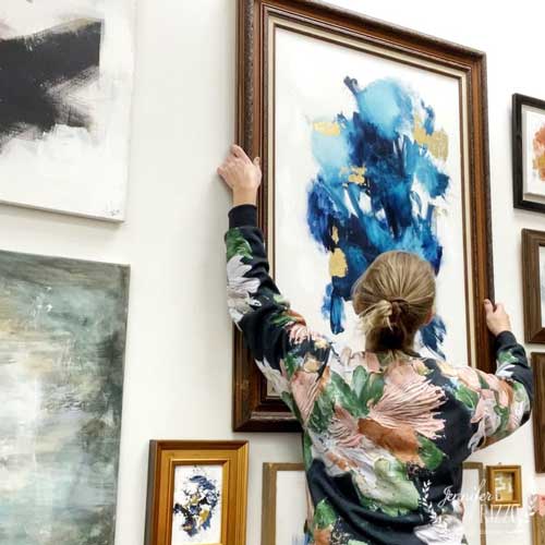 Artist and designer Jennifer Rizzo hangs an abstract canvas painting onto a wall.