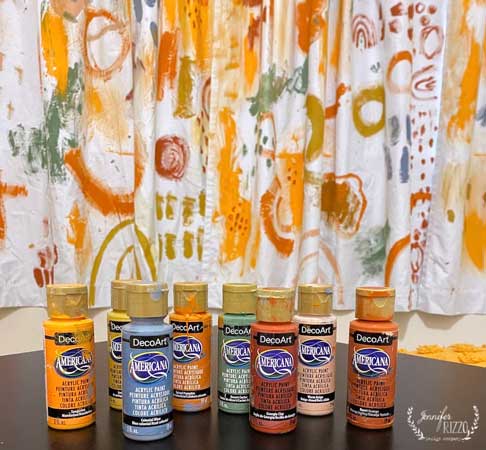 Bottles of DecoArt acrylic paint in front of curtains freshly painted in brilliant fall colors.