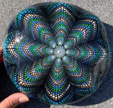 A glossy large stone painted in blue and green dots in a mandala spiral pattern