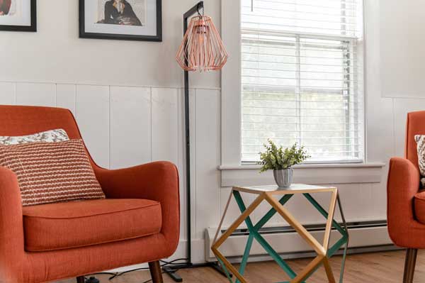 Orange arm chairs sit in a white wood-paneled room.