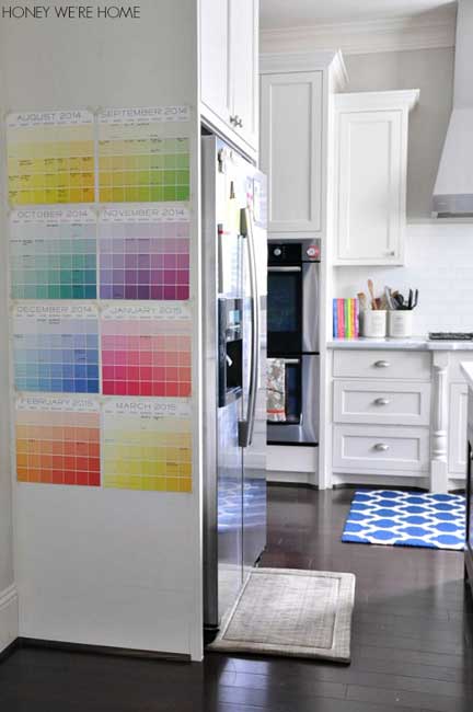 A rainbow of paint chip wall calendar pages on a white kitchen wall.