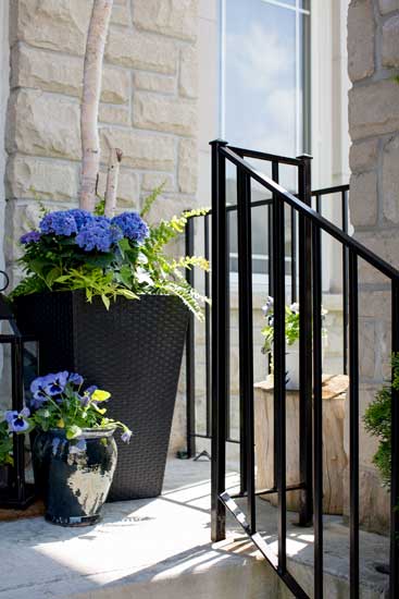 A front porch railing is repainted jet black, and black flower planters are sat next to it filled with blue flowers.