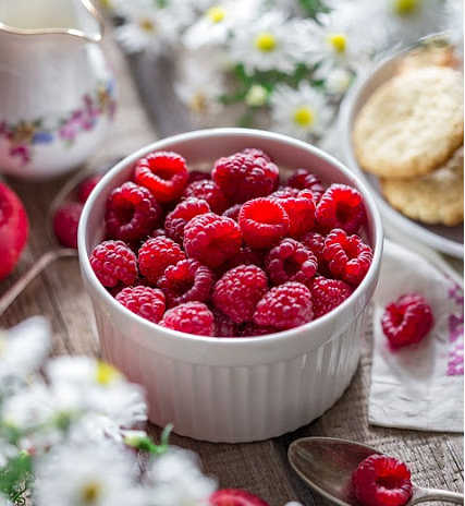 A white bowl is filled with juicy red raspberries