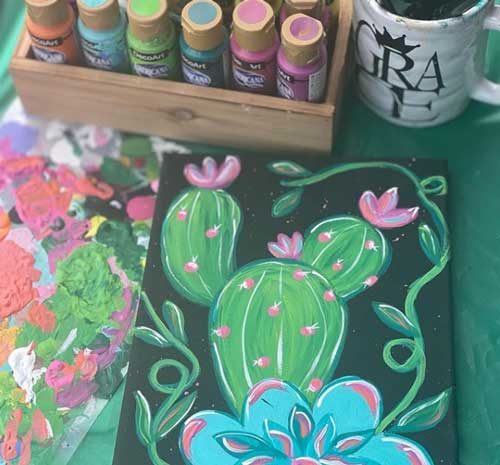 A canvas painting of a cactus with a group of DecoArt's americana acrylics posed next to it.