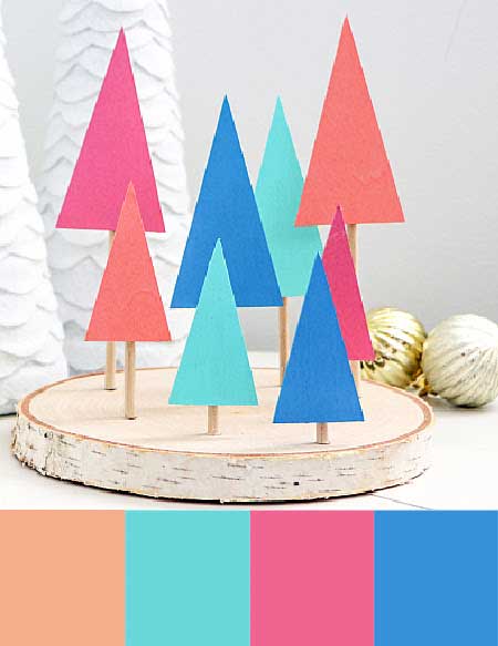 Modern, playful, and colorful christmas decor. Various vibrant colored pieces of paper are cut in a minimal christmas tree shape and placed on top of a wood round to create a bright forest.