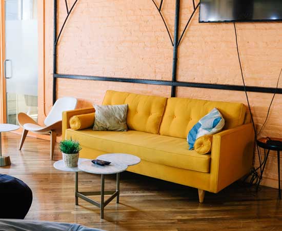 A marigold yellow couch is pushed up against a brick wall in a stylish living room.