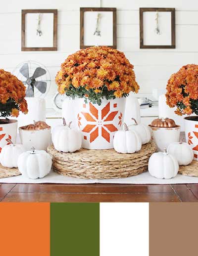 Orange mums are in orange and white pots placed on a dining table. Underneath is a color palette with orange, olive green, white, and soft brown.