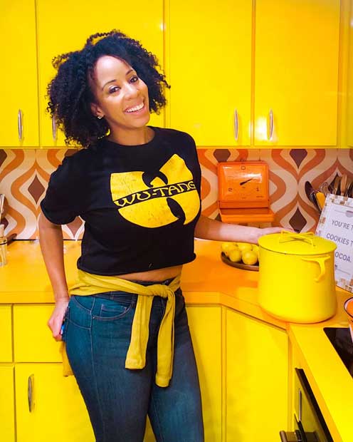 A.V. stands in front of a yellow kitchen with a black and yellow outfit on