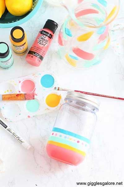 A mason jar is in the middle of being painted with a colorful design using DecoArt glass paint.