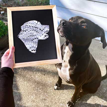 A picture of a black lab dog proudly posing next to a painting of her face