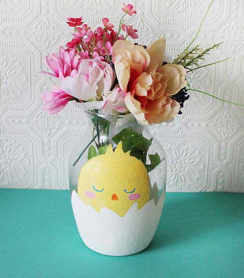 A glass flower vase has a hatching chick painted on it