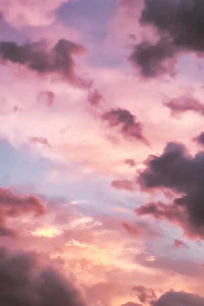 An upward view of the sky during a sunset. The sky is cloudy and filled with pinks and yellow sunlight.
