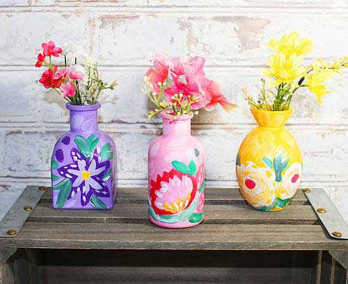 Three vases are painted in floral patterns. One pink, one purple, and one yellow.