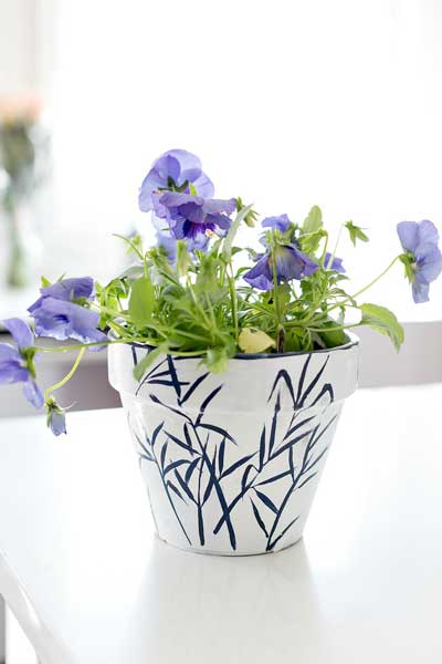 A flower planter is painted white with a minimalist black bamboo leaf pattern elegantly painted on it.