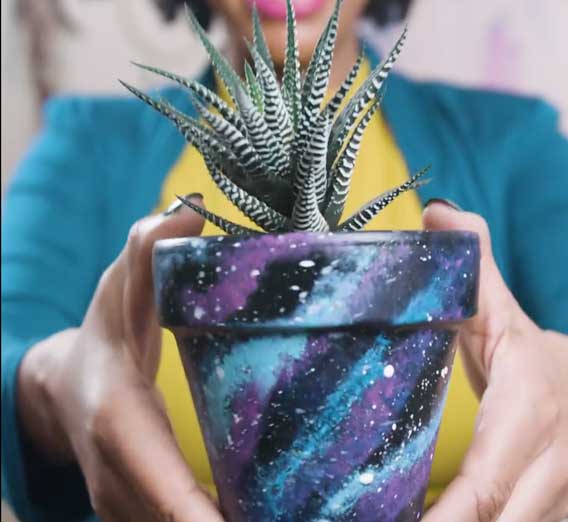 DIY blogger A.V. Perkins holds up a planter she's used scrylic paints to cover in a shimmery galaxy print.