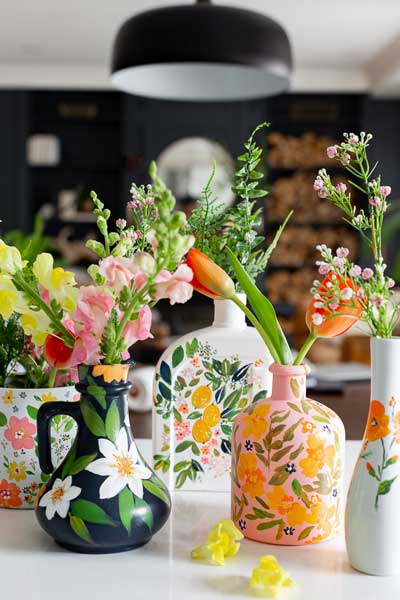 A variety of flower vases with bright florals painted on them using glass paint.