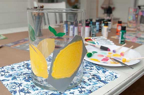 A flower vase has a lemon shaped stencil on it used to paint a lemon on the glass.
