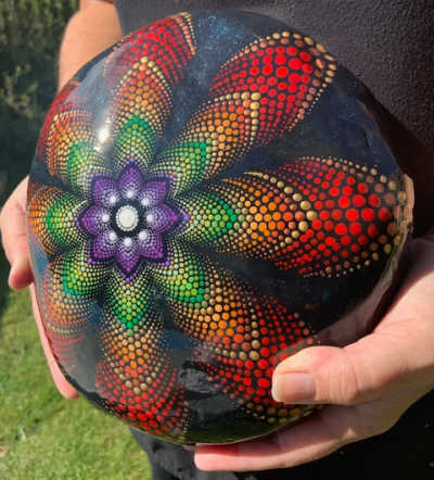 A person holding a large stone painted in a red mandala pattern