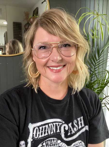 A headshot of Jennofer Rizzo, a smiling blonde woman with wavy hair and a black Johnny Cash t shirt.