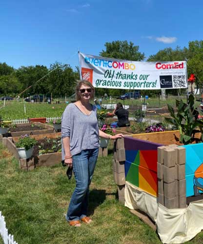 Artist Jennifer Rizzo stands in front of painted garden beds smiling.