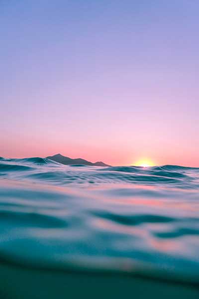 A photo of the ocean, half in and half out of the water. The sun is setting overhead and filling the sky with pink light.