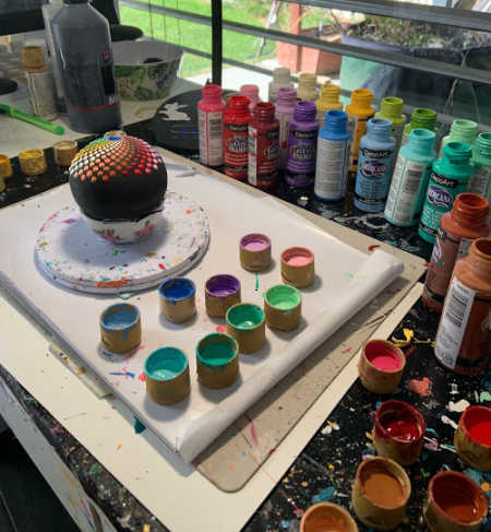 A picture of a rainbow mandala rock in progress next to open bottles of DecoArt Gloss Enamels