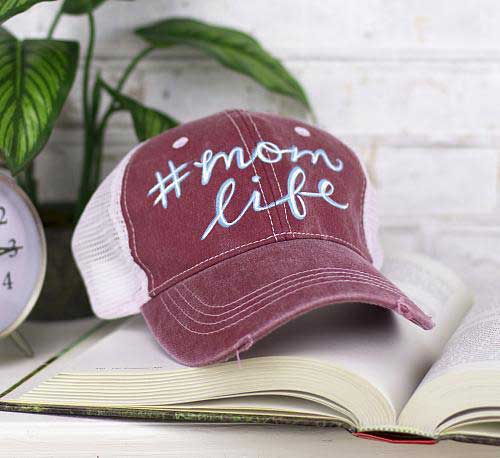 A baseball cap has hashtag mom life painted on it using DecoArt's so soft fabric paint