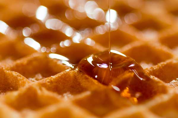 A golden brown waffle with maple syrup being drizzled on it.