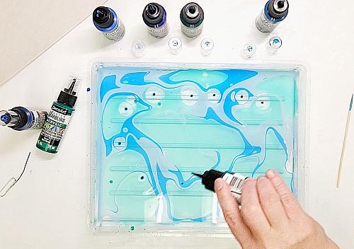 An artist uses DecoARt water marbling acrylics to create a swirling blue pattern