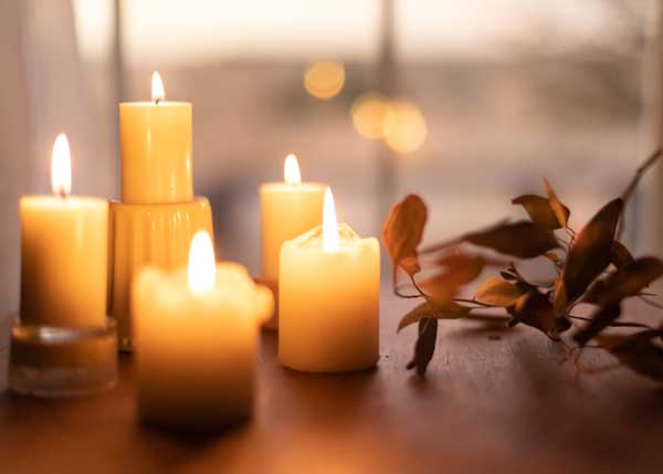 Several candles on a table next to some fall leaves all bathed in a golden light