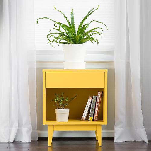 An end table painted in marigold yellow with a potted plant on top of it.